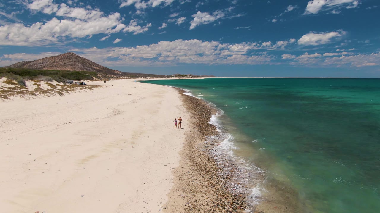 Two people continue along the beach as small waves reach the shoreline.