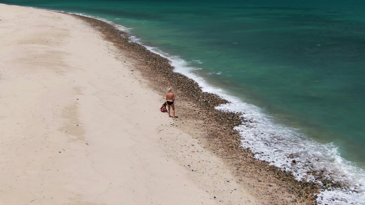 Person standing by rocky edge where small waves meet the sand.