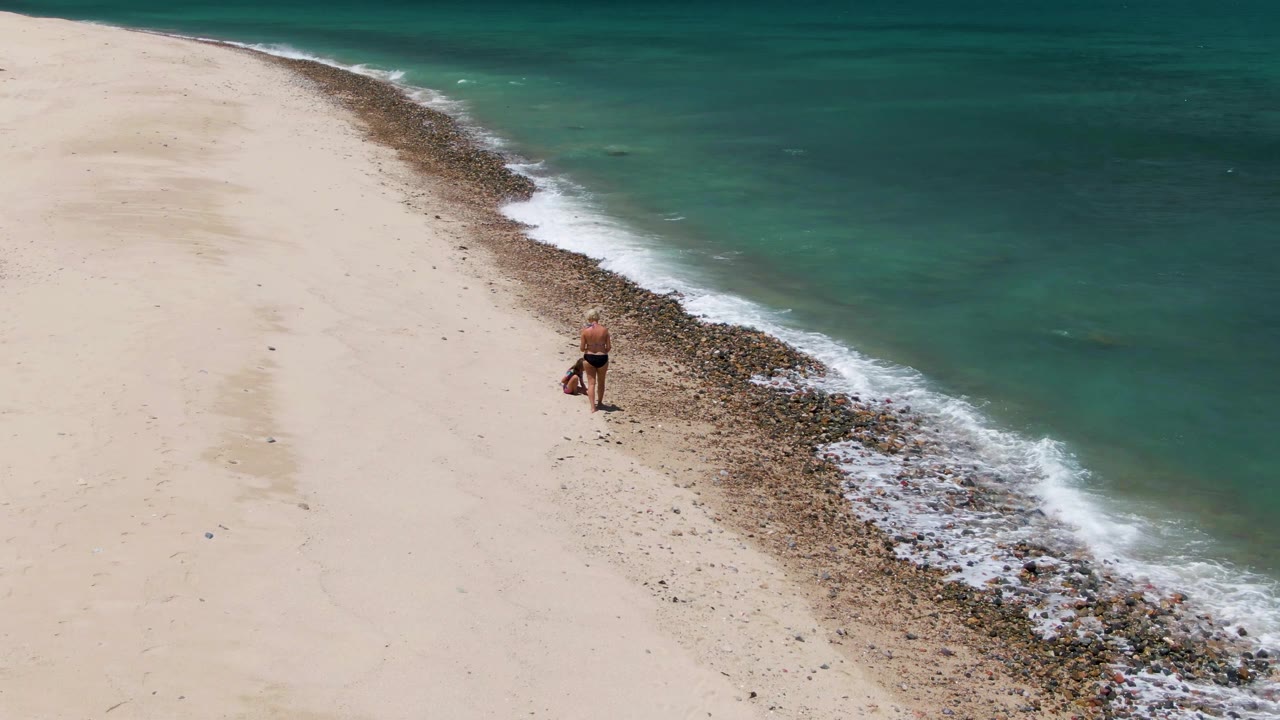 At Barakas Beach in Baja California Sur, the person remains near the curved rock band as fresh white foam spreads farther along the turquoise waterline.