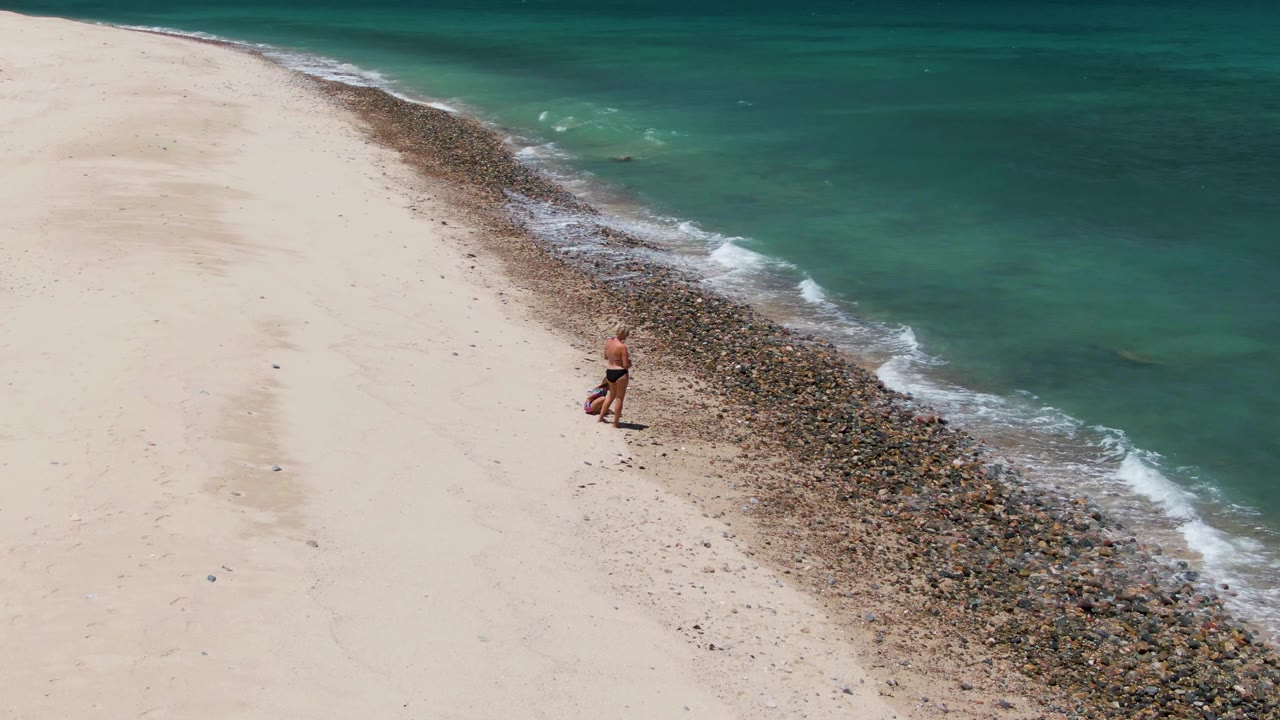 Adult on sandy beach near rocks and turquoise surf