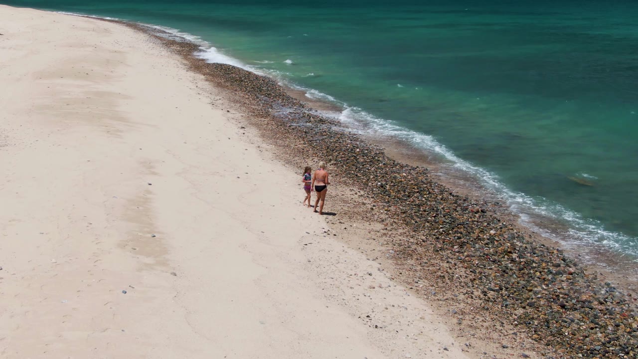 Adult and child walking along a rocky sandy beach