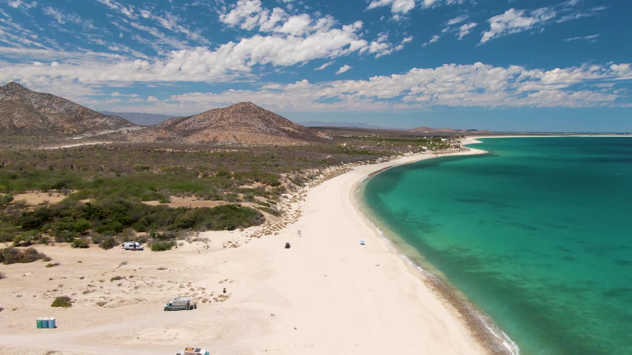 White beach and turquoise water seen from above with vehicles on the sand.
