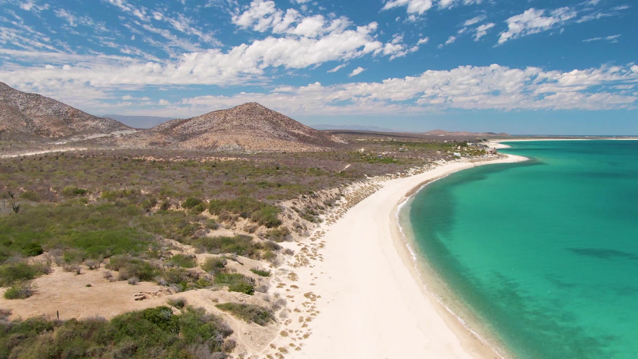 Aerial view of white sand beach, turquoise water, dry scrub, and low hills.
