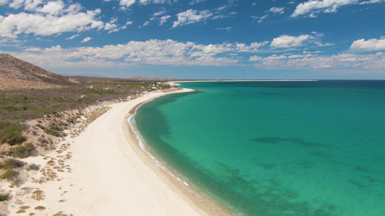 Aerial view of a curved white sand beach beside turquoise ocean water.