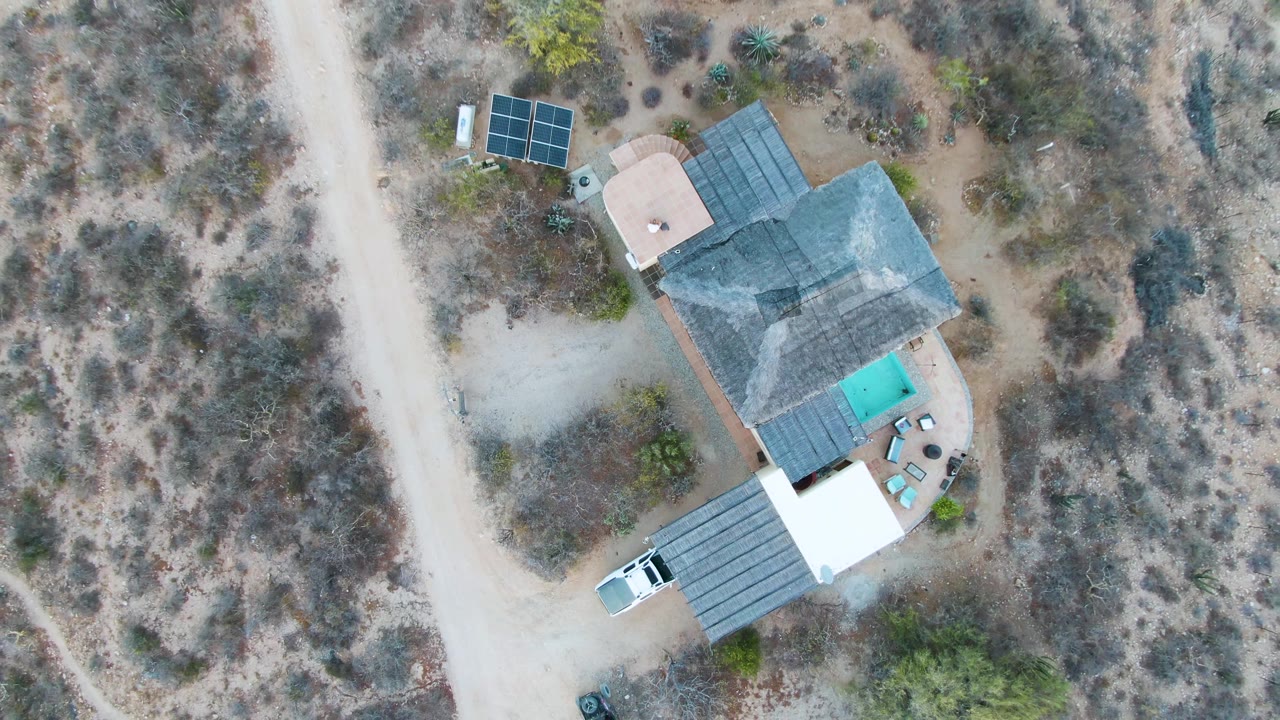 Drone frame of the house with the dirt road and surrounding arid vegetation.