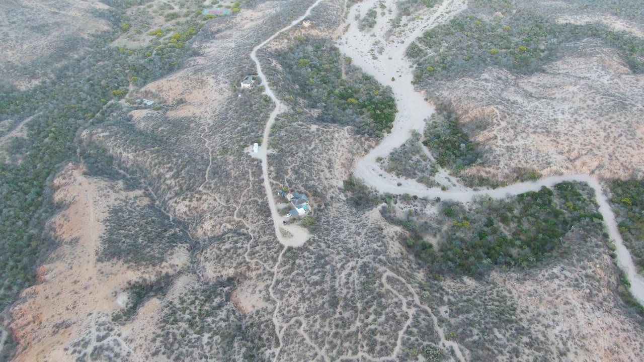 Dirt road curves past low vegetation and a small structure.