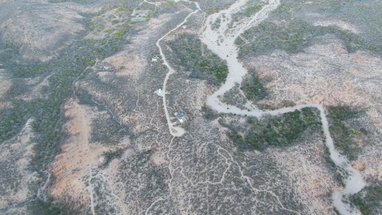 Aerial view of a car on a pale winding dirt road through dry hills.