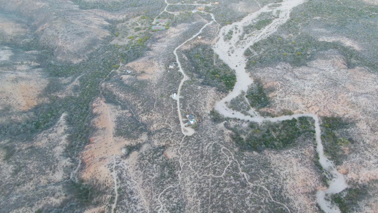 At one second, the drone view keeps the small vehicle near the lower left dirt track as the dry riverbed branches through Cabo Pulmo hills with no visible people.