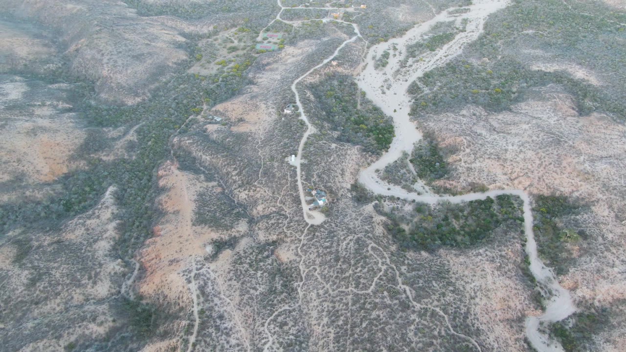At two seconds, the aerial composition shows the winding dirt road curving past green scrub and a dry wash in Cabo Pulmo, with the vehicle still small and no visible people.