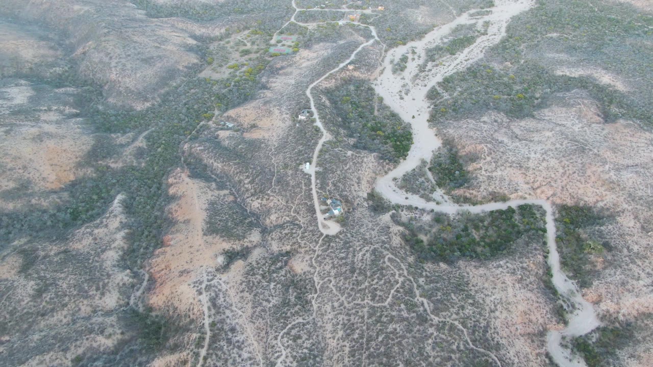 Aerial shot of a vehicle beside a dry riverbed in scrub-covered hills.