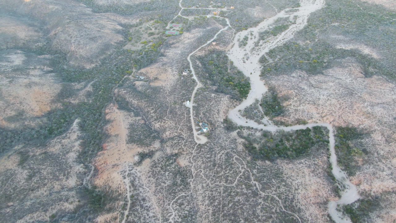 Aerial view of a pale dry riverbed crossing scrubby arid hills.