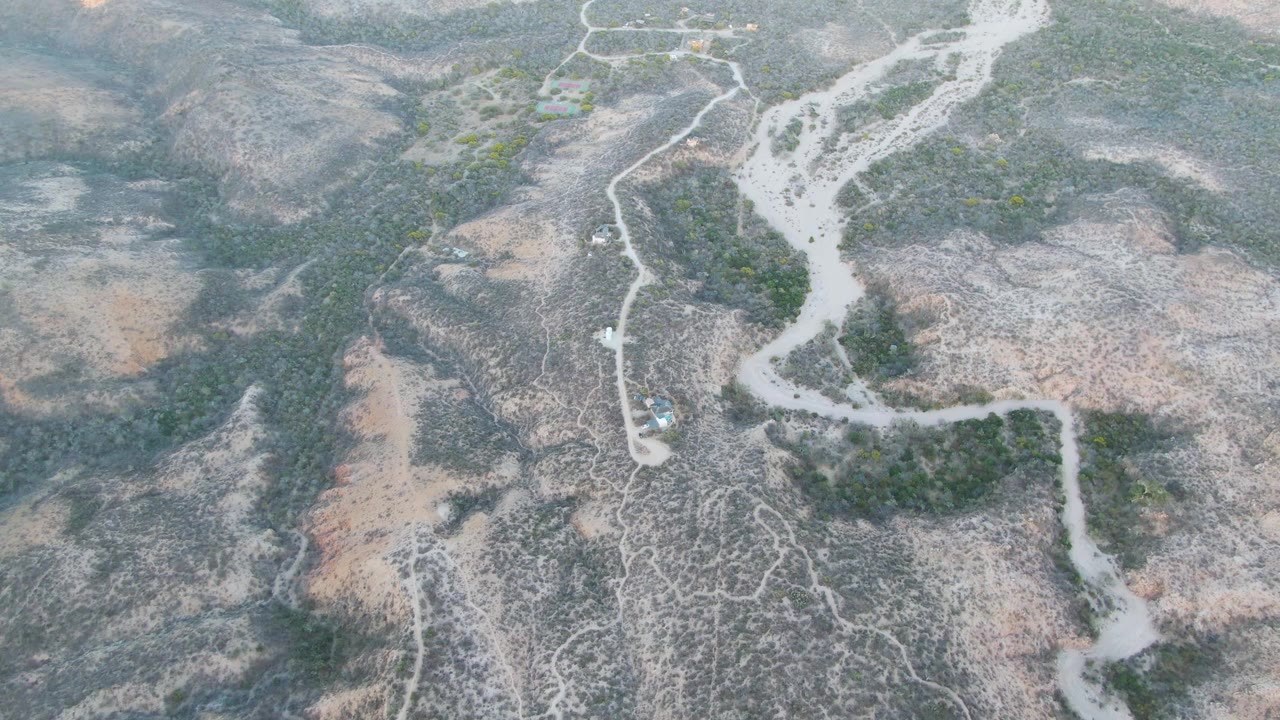 Drone-height view near Cabo Pulmo, Baja California Sur, with branching pale washes crossing gray-brown terrain, scrub patches, and no visible people.