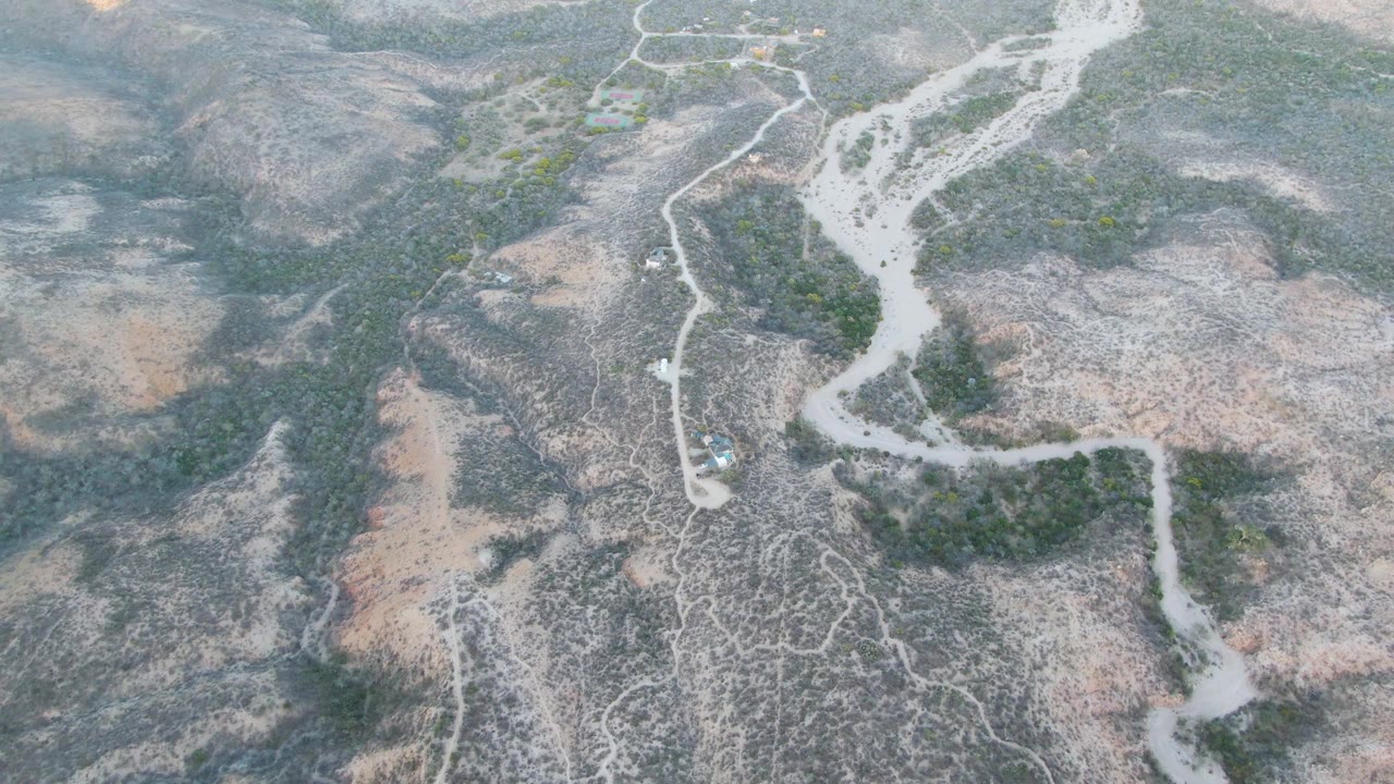Aerial frame near Cabo Pulmo, Baja California Sur, showing the dry channel bending through low hills, with scrub vegetation scattered across exposed earth and no visible people.