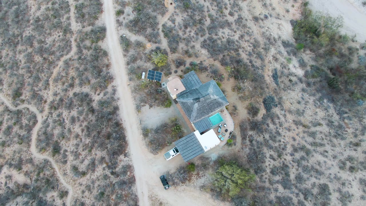 Overhead desert property with solar panels, pool, driveway, and dry vegetation.