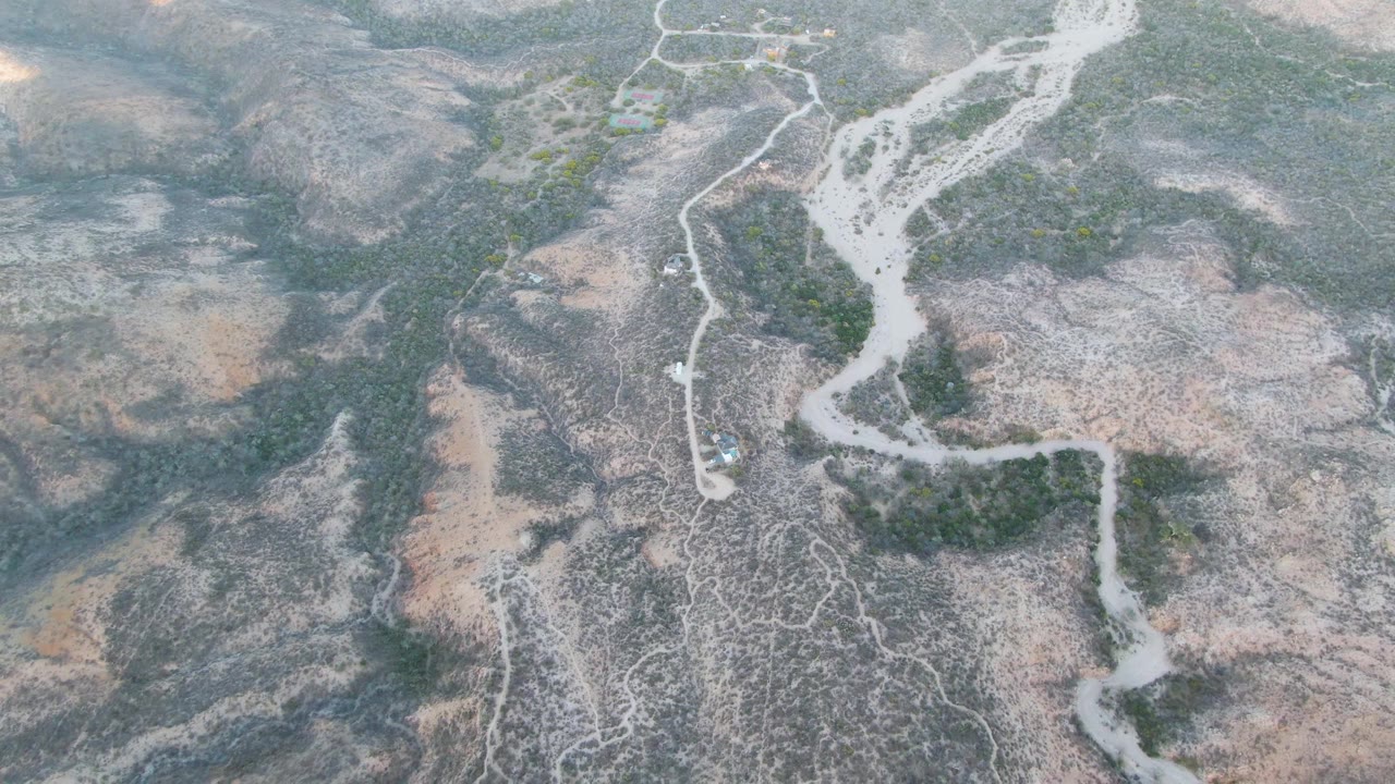 Aerial view of a dry riverbed and scrub-covered arid hills.