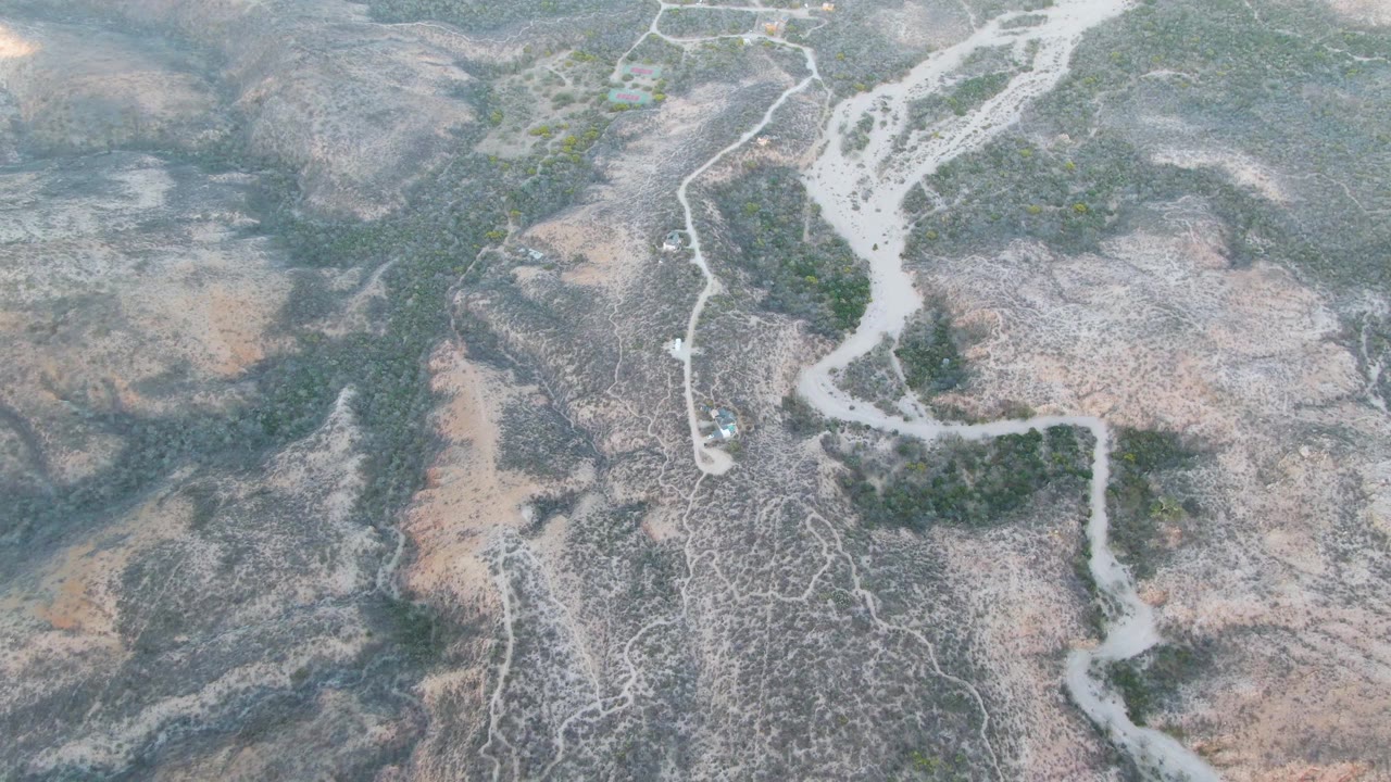 Aerial frame in Cabo Pulmo, Baja California Sur, with the dry waterway running diagonally through scrubby gray and tan terrain and no visible people.
