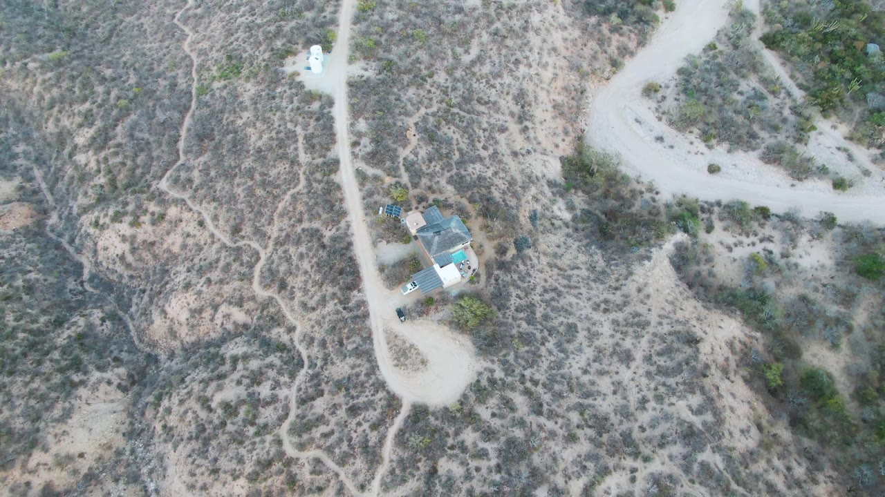 Dry hillside with a dirt road, a house, and a white vehicle seen from above.