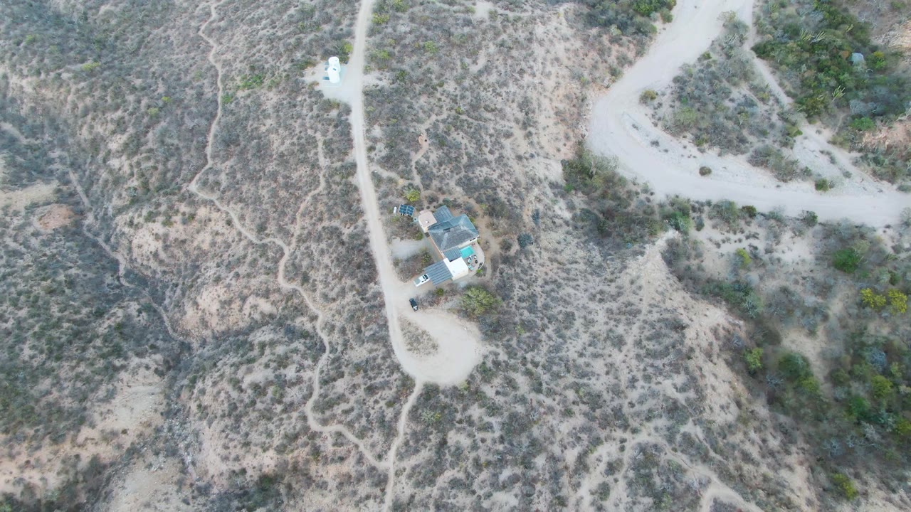 Aerial view of desert road curving past scrubland and a small house