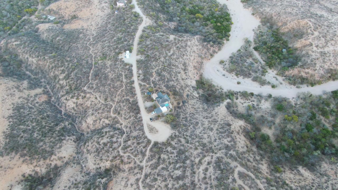 Overhead Cabo Pulmo view with the white car on the pale road, dry gullies and footpaths crossing the hillside, and no visible people.
