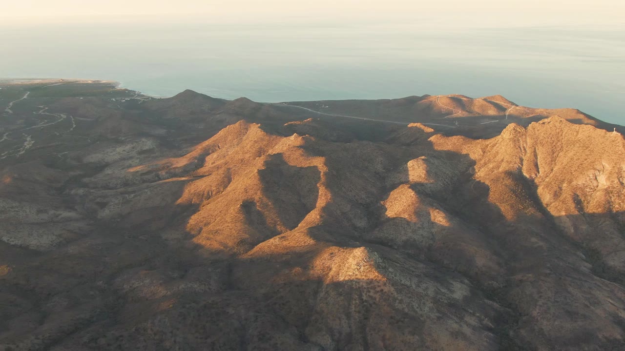 Sunlit rocky mountain ridges with ocean on the horizon.