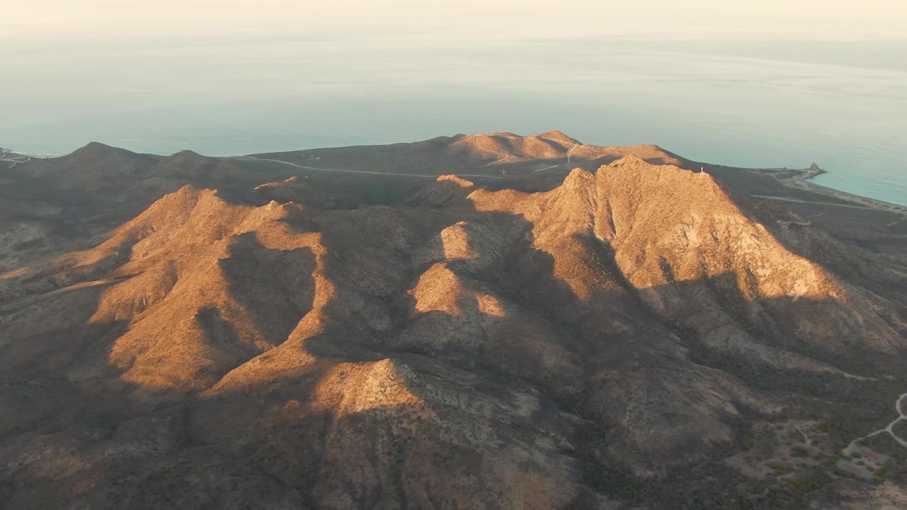 Warm low-angle light crosses the rocky hills near Cabo Pulmo, with the ocean and coastline in the background and no visible people.