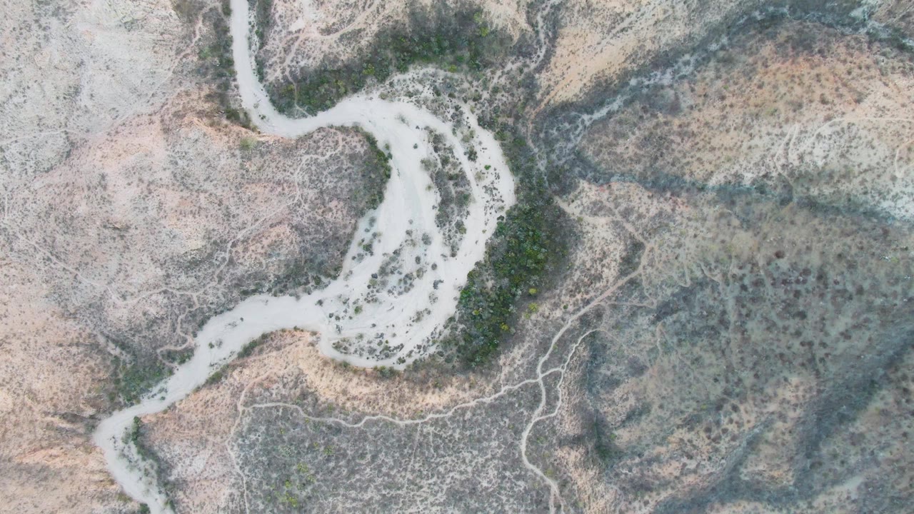 Overhead view of a pale winding riverbed through dry terrain