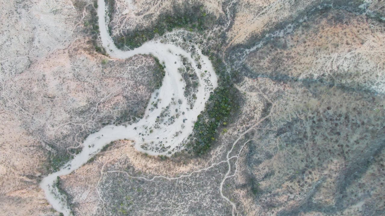Aerial frame from Cabo Pulmo, Baja California Sur showing the sandy river bend more centered, with a green vegetation patch along one edge and no visible people.