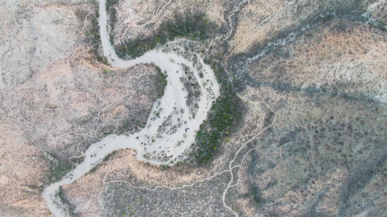 Overhead frame from Cabo Pulmo, Baja California Sur showing the curving dry river channel against mottled scrub-covered ground, with no visible people or structures.