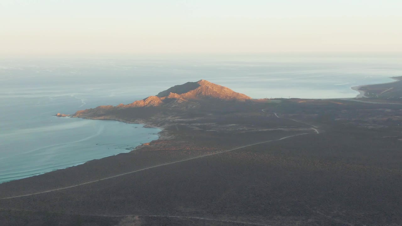 Aerial view of coastal mountain, ocean, dry terrain, and winding road