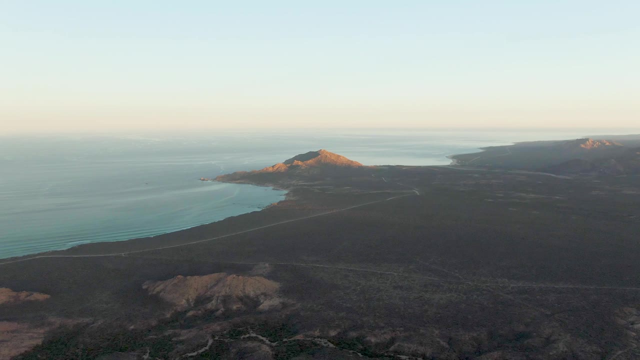 Aerial view across ocean, coastal road, and dark hills