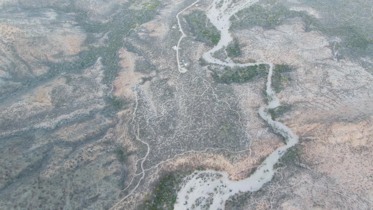 Top-down aerial of a winding pale river channel through dry hills.
