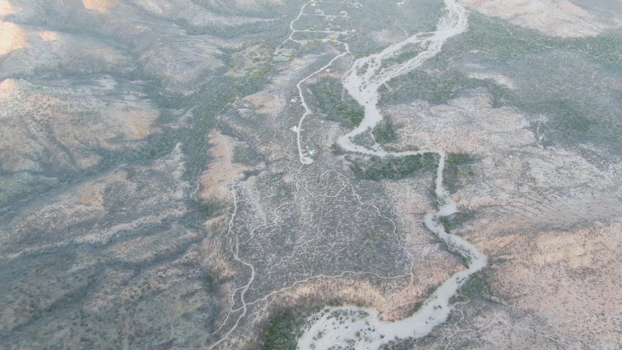 Aerial view in Cabo Pulmo, Baja California Sur, with branching pale washes, gray-brown ridges, sparse green scrub, and no visible people.