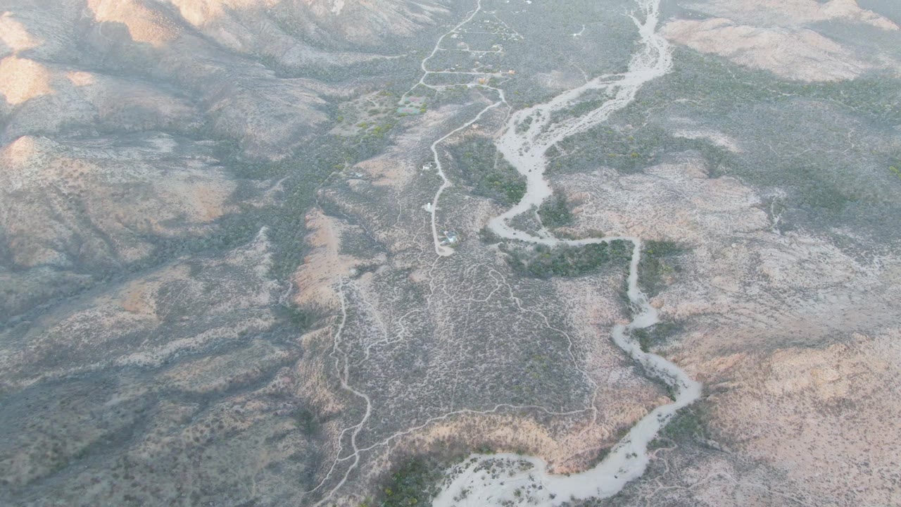 Aerial shot of a meandering riverbed below shadowed rocky ridges.
