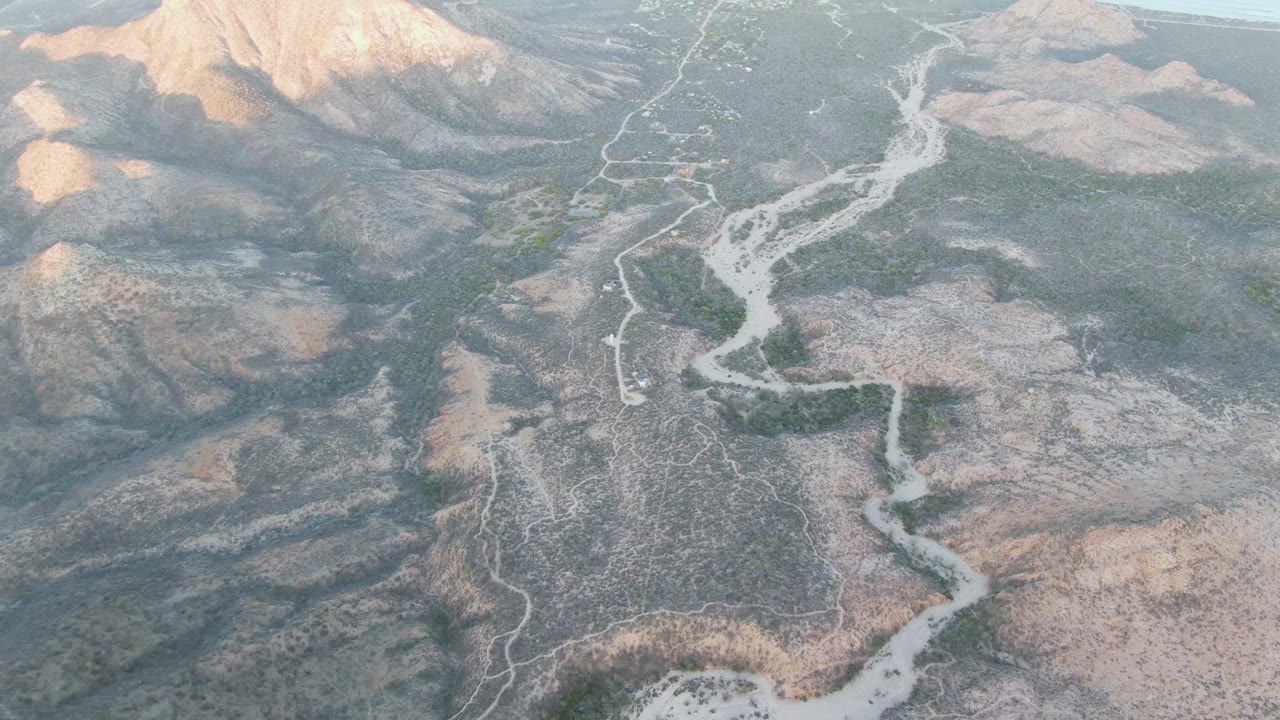 Aerial view of rocky desert hills with a winding pale road and dry riverbed.