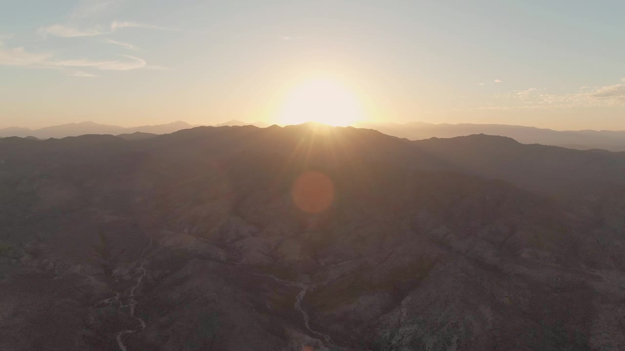 Bright sun over layered desert mountains and shadowed canyons