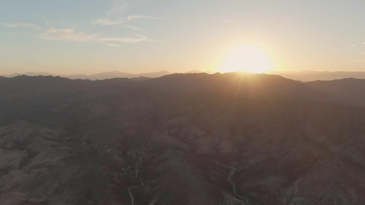 Aerial view over Cabo Pulmo's arid canyon floor as the low sun brightens the ridge line and distant mountain layers, with no visible people.