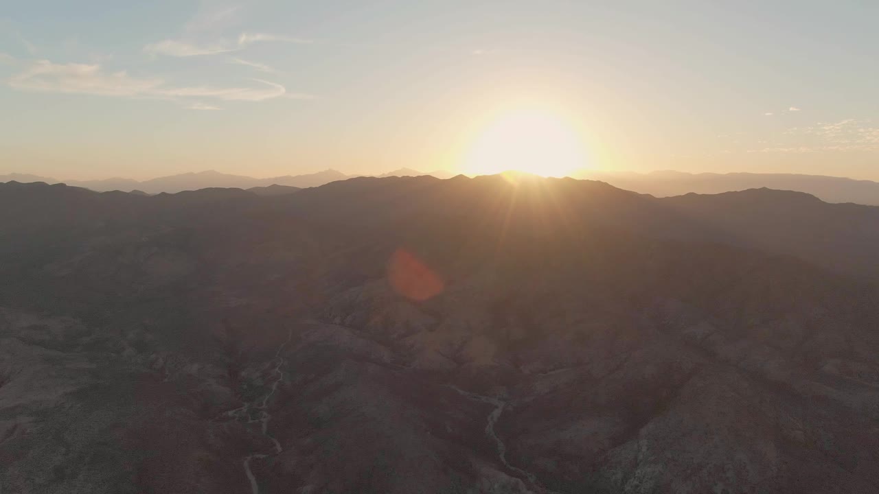 Bright sun centered above layered mountains and shadowed valley terrain
