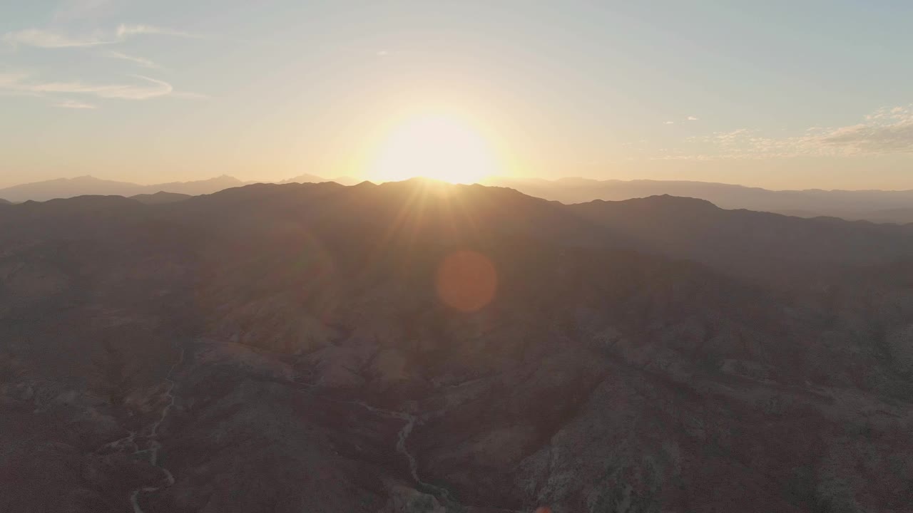 Sun low over dark mountain valley with winding river below.