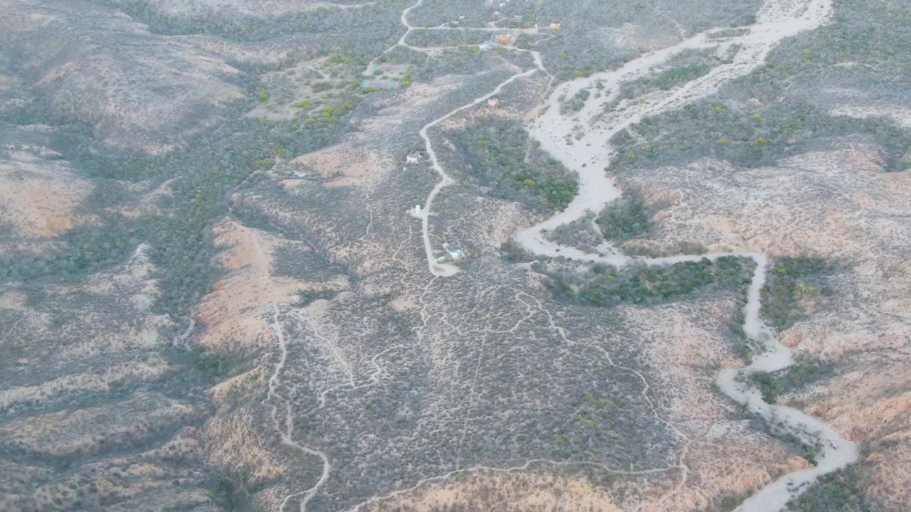Overhead view of a pale winding riverbed through dry hills