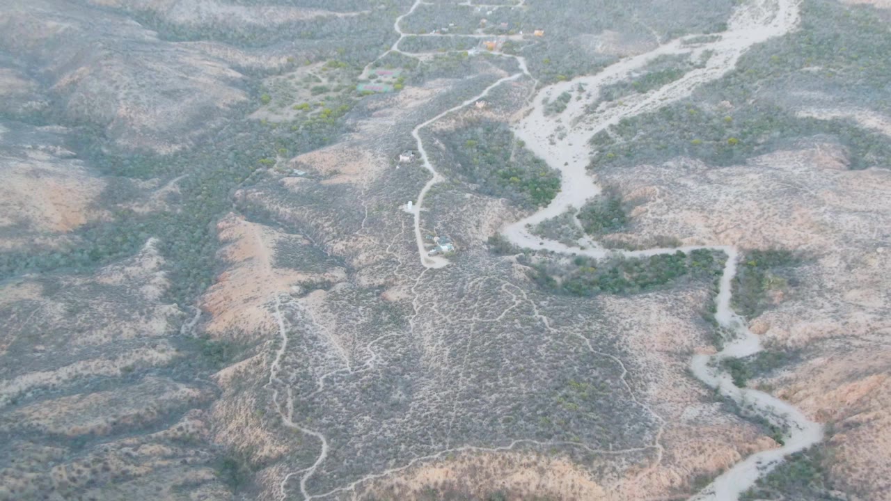 Aerial frame from Cabo Pulmo, Baja California Sur with a branching pale wash and winding riverbed framed by dry ridges, scrub patches, and no visible people.
