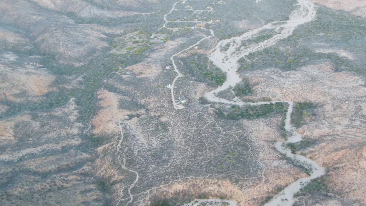 Drone-style aerial frame from Cabo Pulmo, Baja California Sur showing the river channel bending between dry hills, with darker scrub along the banks and no visible people.