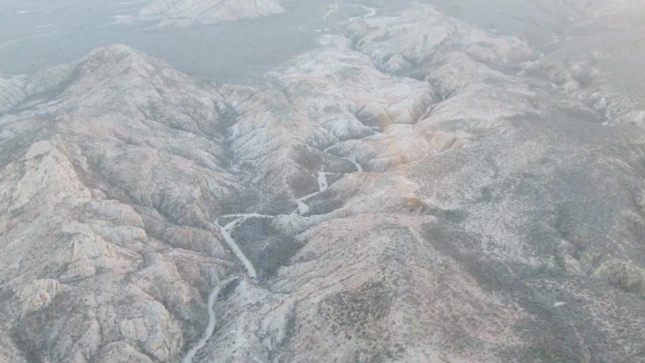 Aerial mountain valley with pale ridges, haze, and stream channel