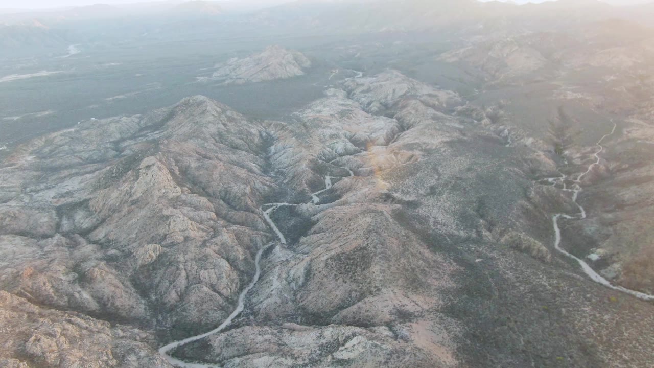 High aerial view of rugged hills with a winding pale channel leading through the foreground.