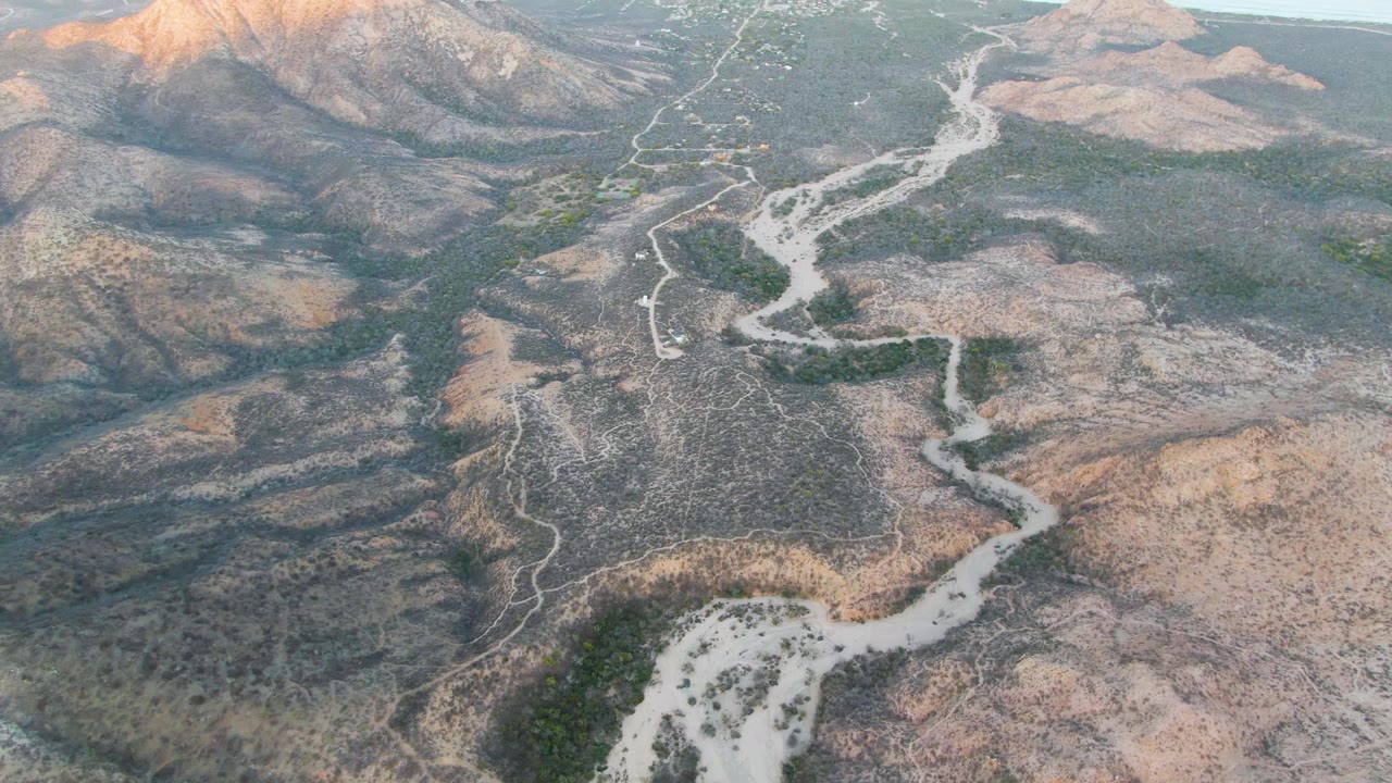 Aerial view of a winding dirt road through dry mountain terrain.
