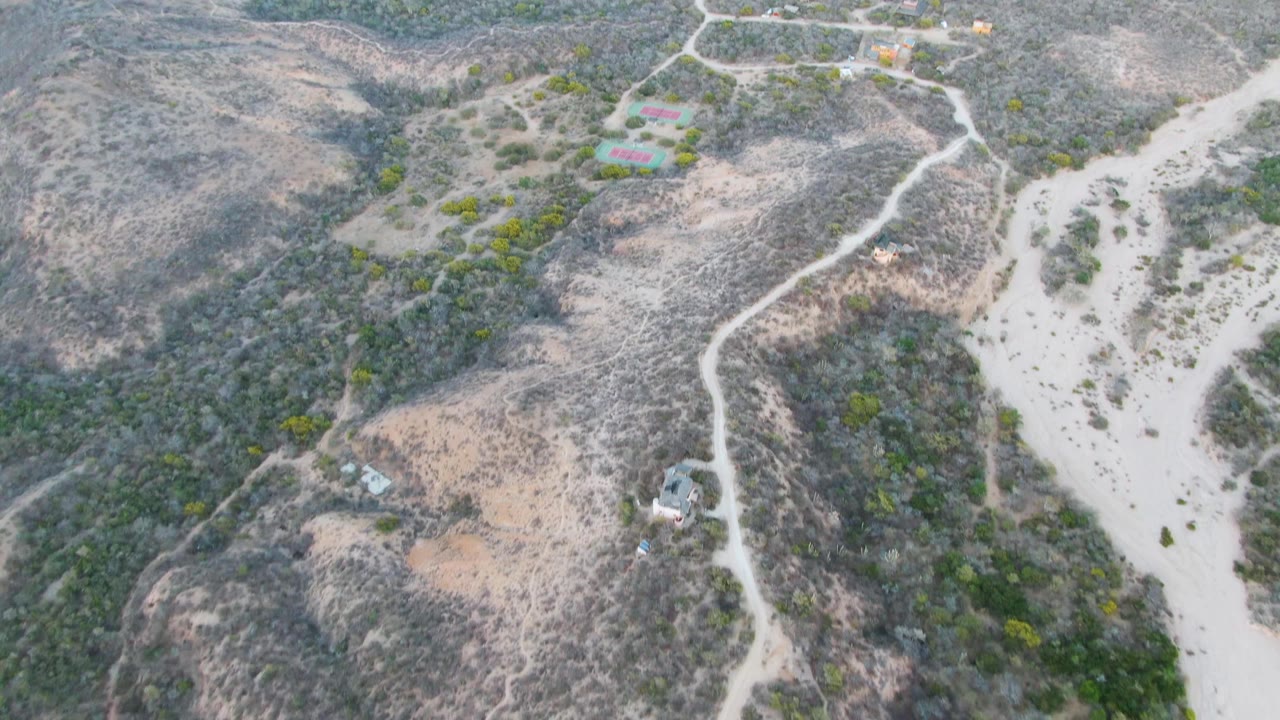 Drone view over rocky hills with dirt tracks and small structures.