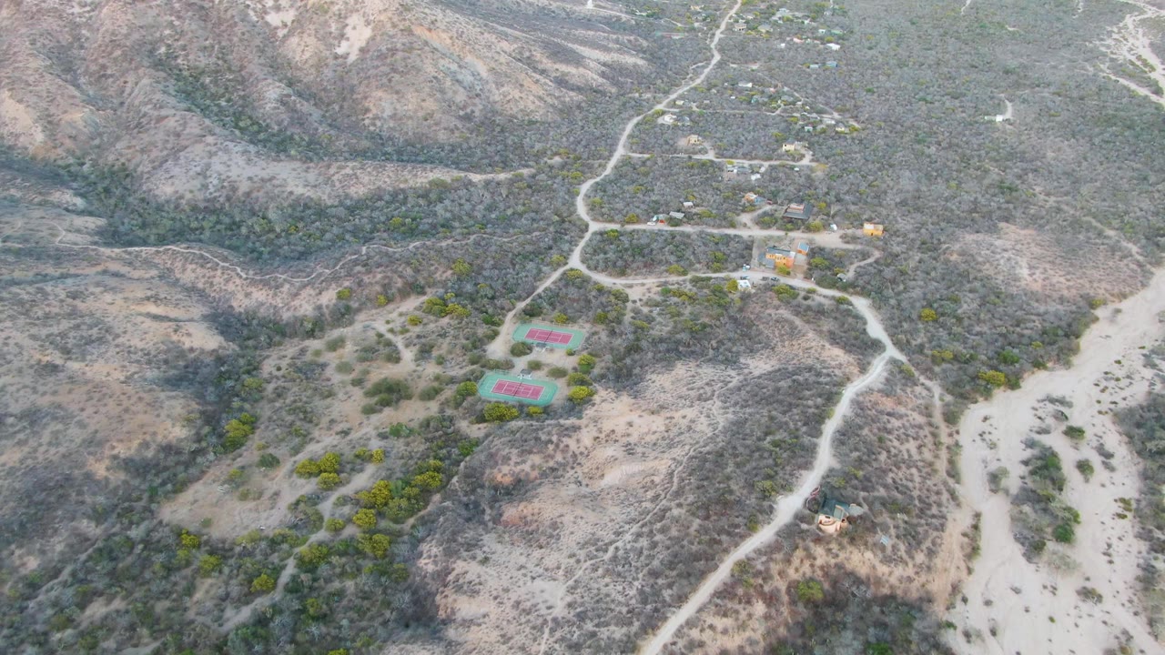 Aerial frame of dirt roads crossing dry hills near small buildings