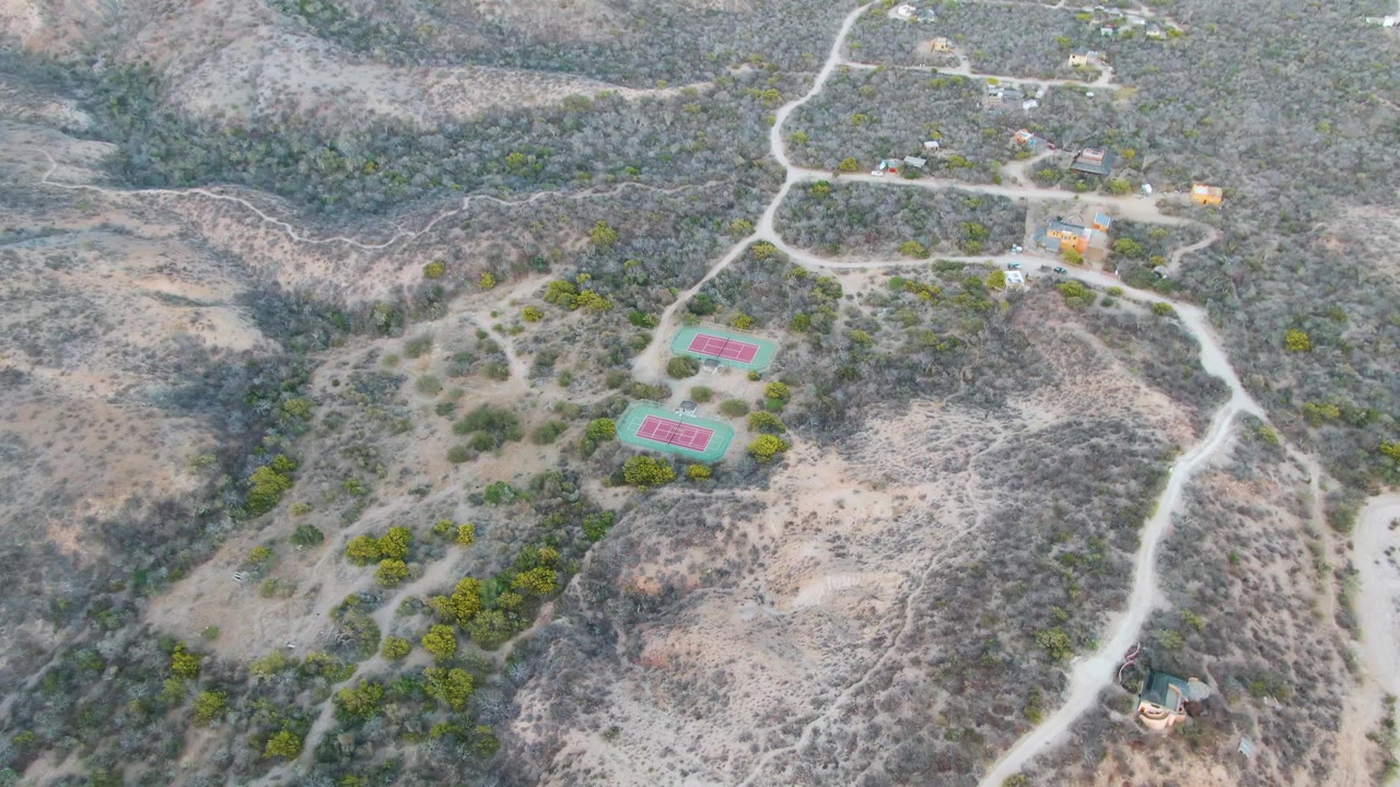 Aerial landscape with tennis courts, scrub hills, and dirt tracks