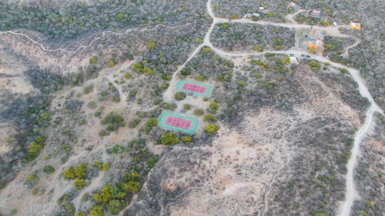 Overhead hillside view with two tennis courts and branching dirt tracks.