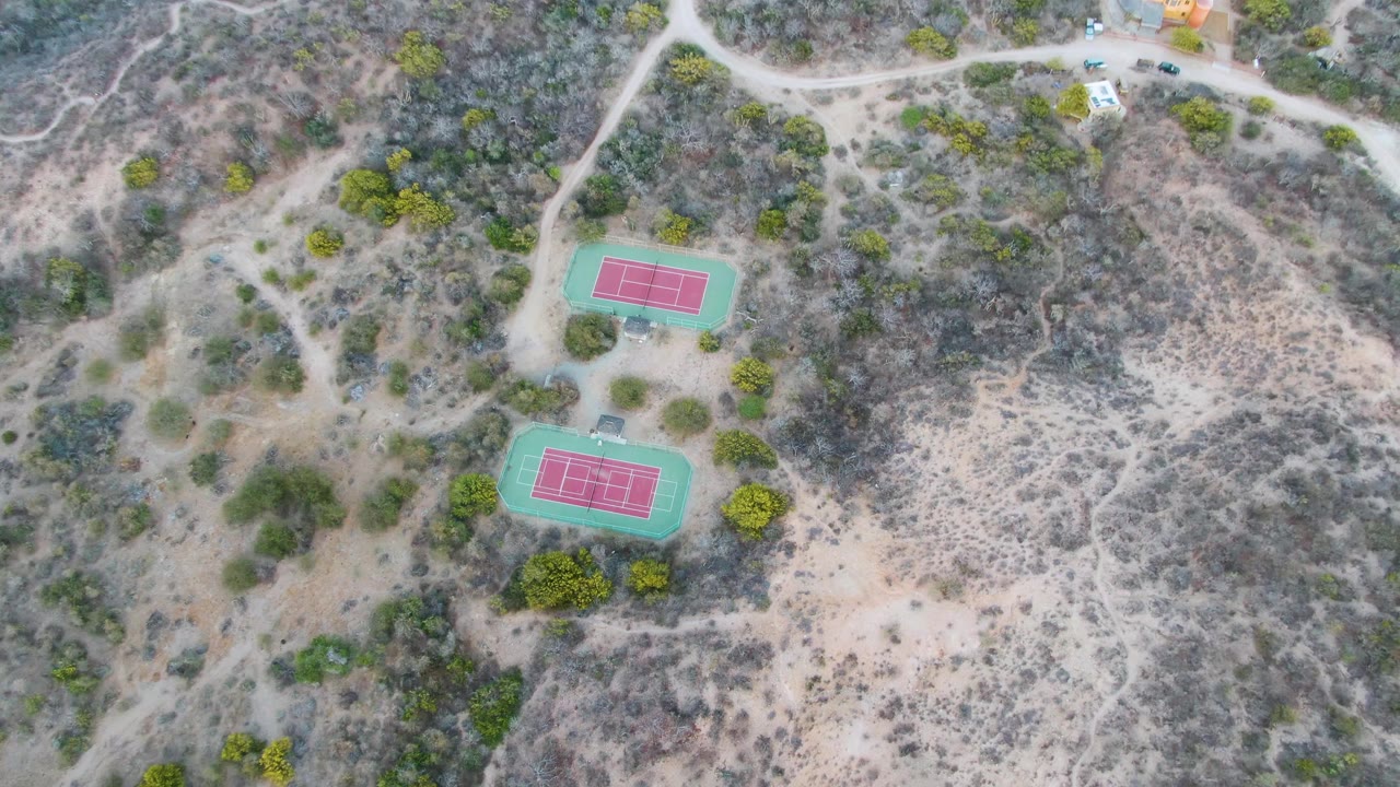 Aerial shot of tennis courts on dusty terrain with roads and trees.
