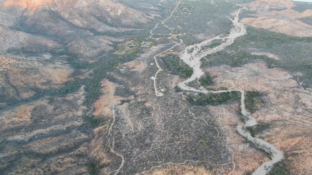 Aerial view of dry hills with a winding pale wash and dirt tracks.
